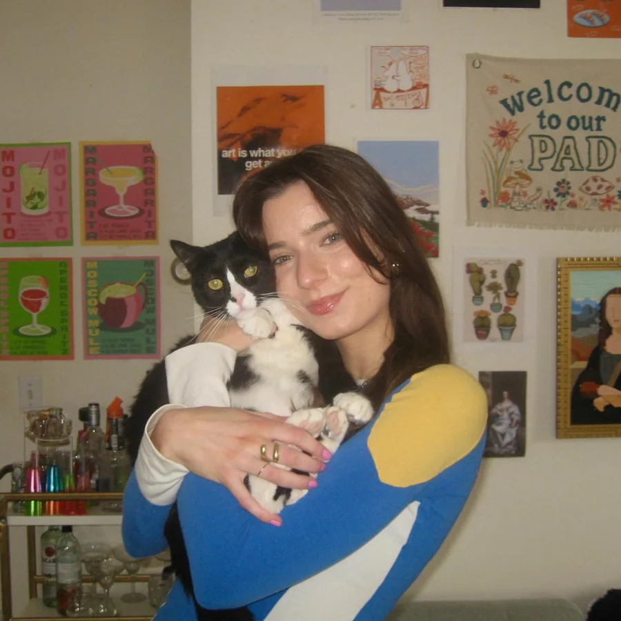 Grace holding her black-and-white tuxedo cat in front of a colorful art-covered wall.