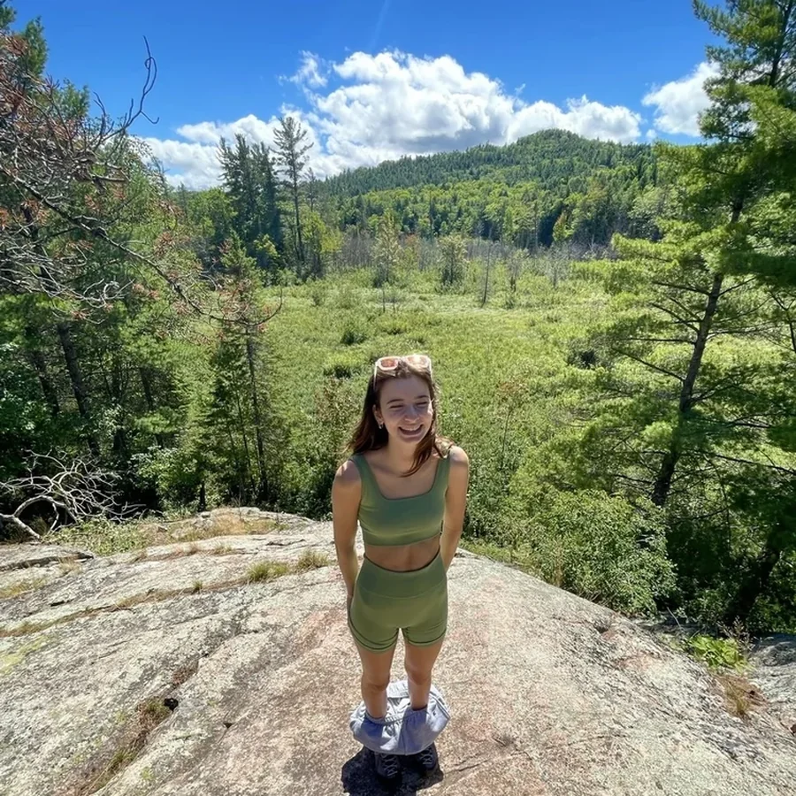 Grace smiling on a rocky overlook above a green valley on a sunny hike.