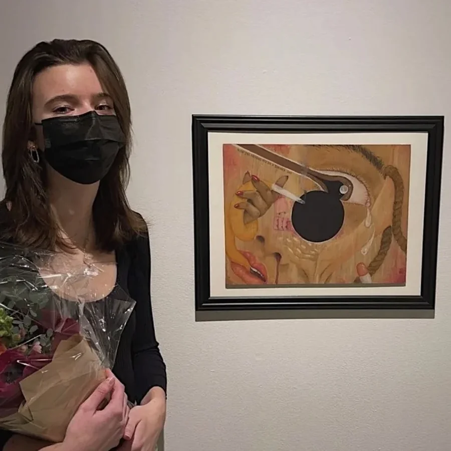 Grace standing beside one of her framed paintings at a gallery exhibition.