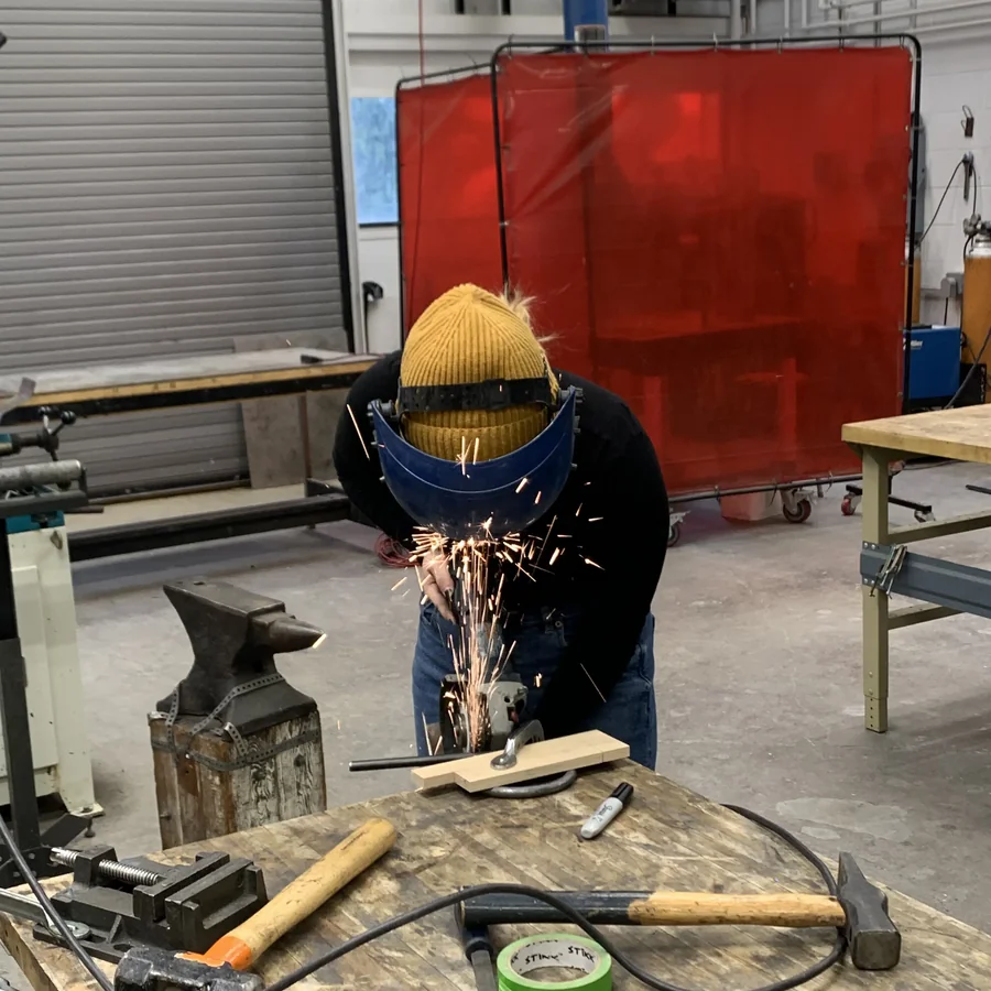 Grace welding, sparks flying, in protective gear.