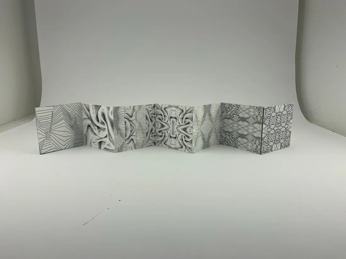 A folded accordion artist book covered in intricate graphite patterns.