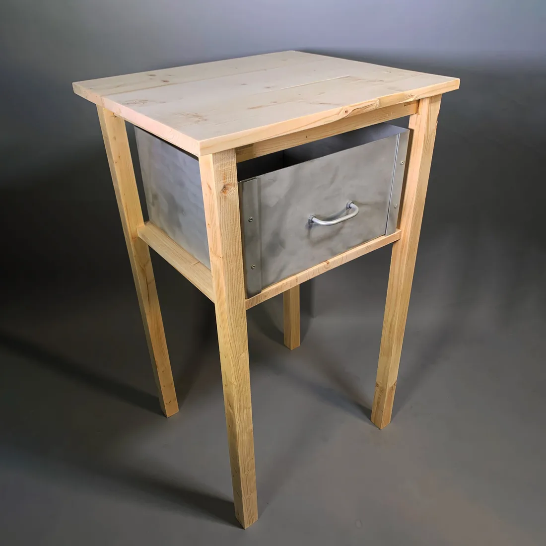 A handmade wooden side table with tapered legs and a metal drawer.