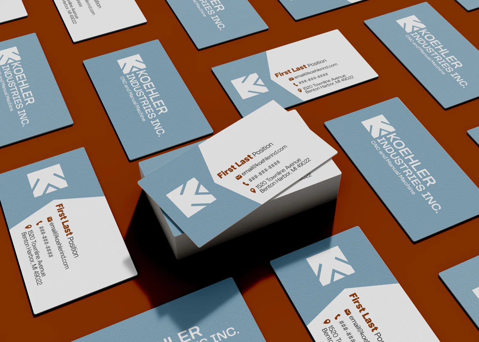 Koehler Industries business cards arranged on a rust-orange surface, in dusty-blue and white, showing the angular K logo, wordmark, and contact details.