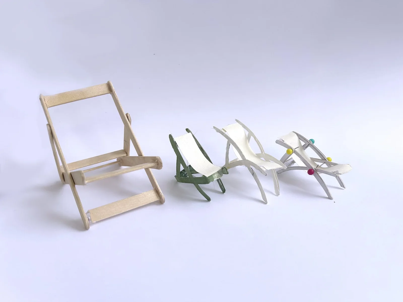 Miniature scale-model chair prototypes made from balsa, paper, and pins, exploring different folding lounge-chair structures and ergonomics.