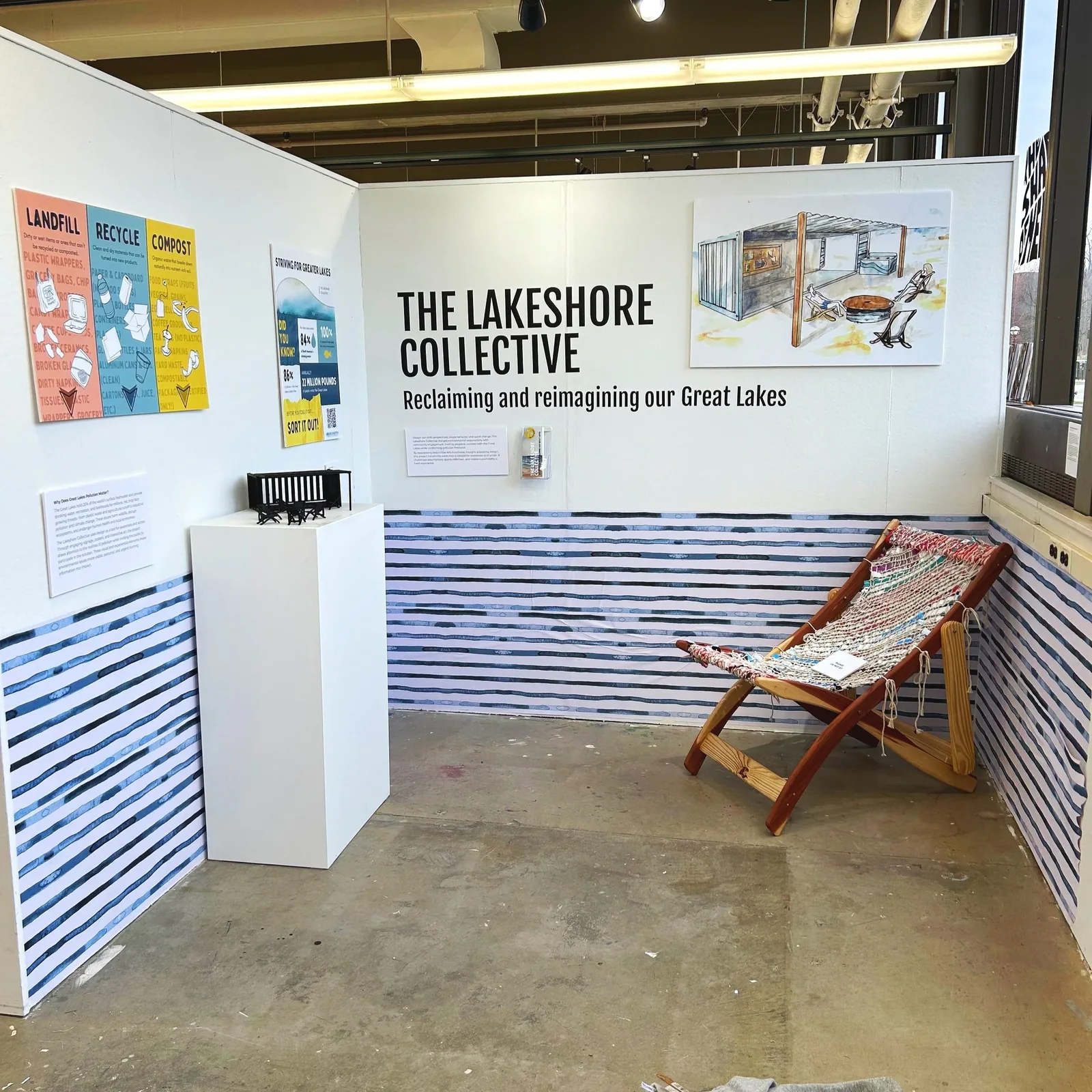 The Lakeshore Collective exhibition booth: a wall headline reading 'Reclaiming and reimagining our Great Lakes,' the spatial rendering, sorting and statistics signage posters, a scale model, and the finished waste-woven chair.