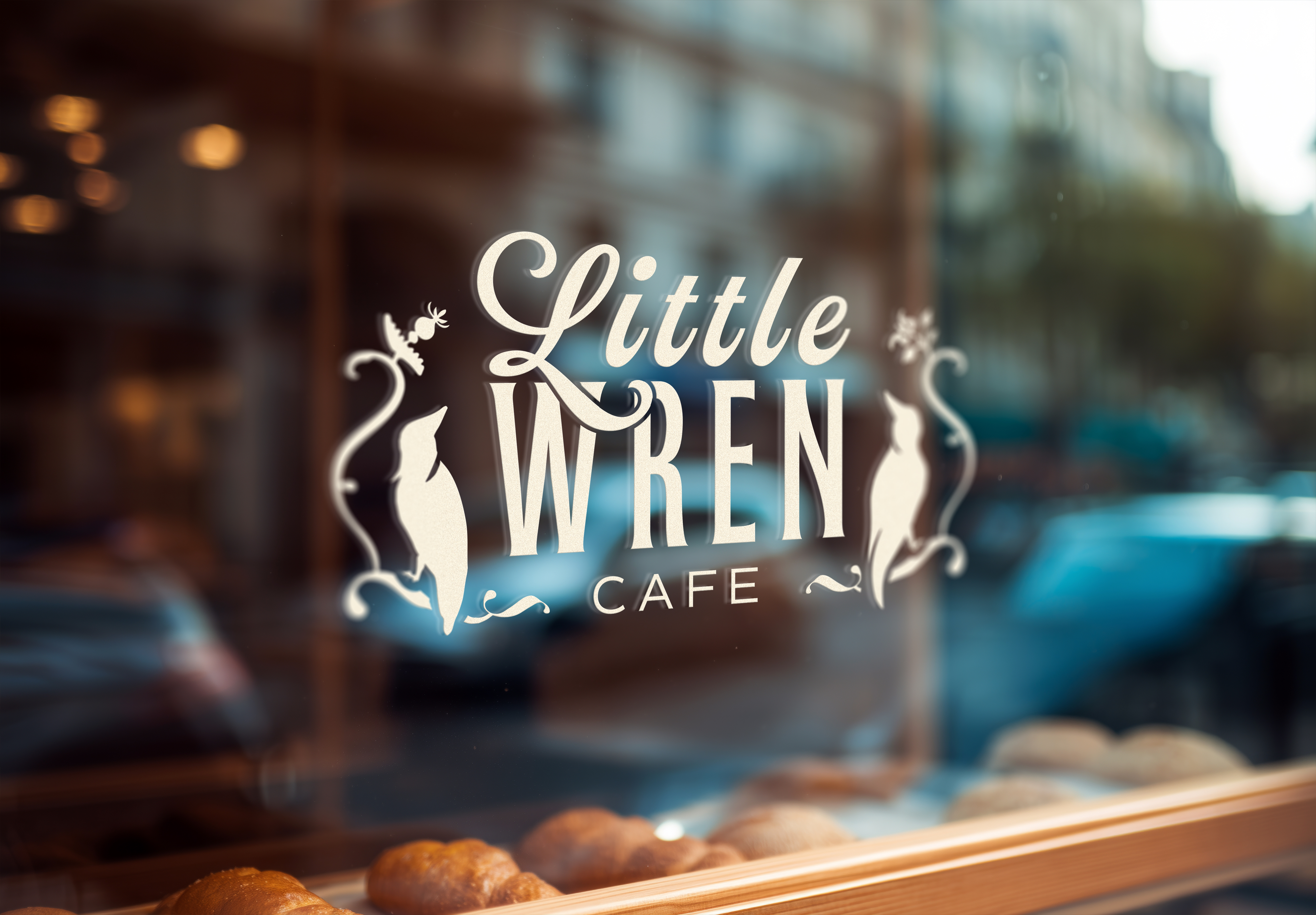 The Little Wren Cafe logo, a script-and-serif wordmark flanked by two perched birds, applied in white vinyl on a sunny café storefront window.
